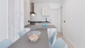 A modern kitchen with a central island, a dining table with chairs, and a large window.