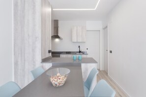 A modern kitchen with a central island, a dining table with chairs, and a large window.