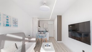 A modern living room with a sofa, a coffee table, a TV, and a dining area with chairs and a table.