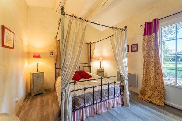 Un lit à baldaquin à quatre poteaux, avec un oreiller rouge, des lampes de chevet et une fenêtre avec des rideaux.