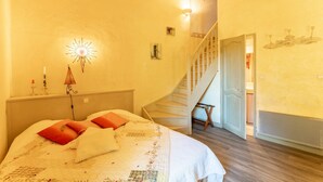 A bedroom with a bed, a nightstand, a wall-mounted lamp, a staircase, and a door leading to another room. - Provençal Gîte "La Rivière" – 4 Bedrooms, Private Terrace, Pool & Garden by the Sorgue (Velleron)