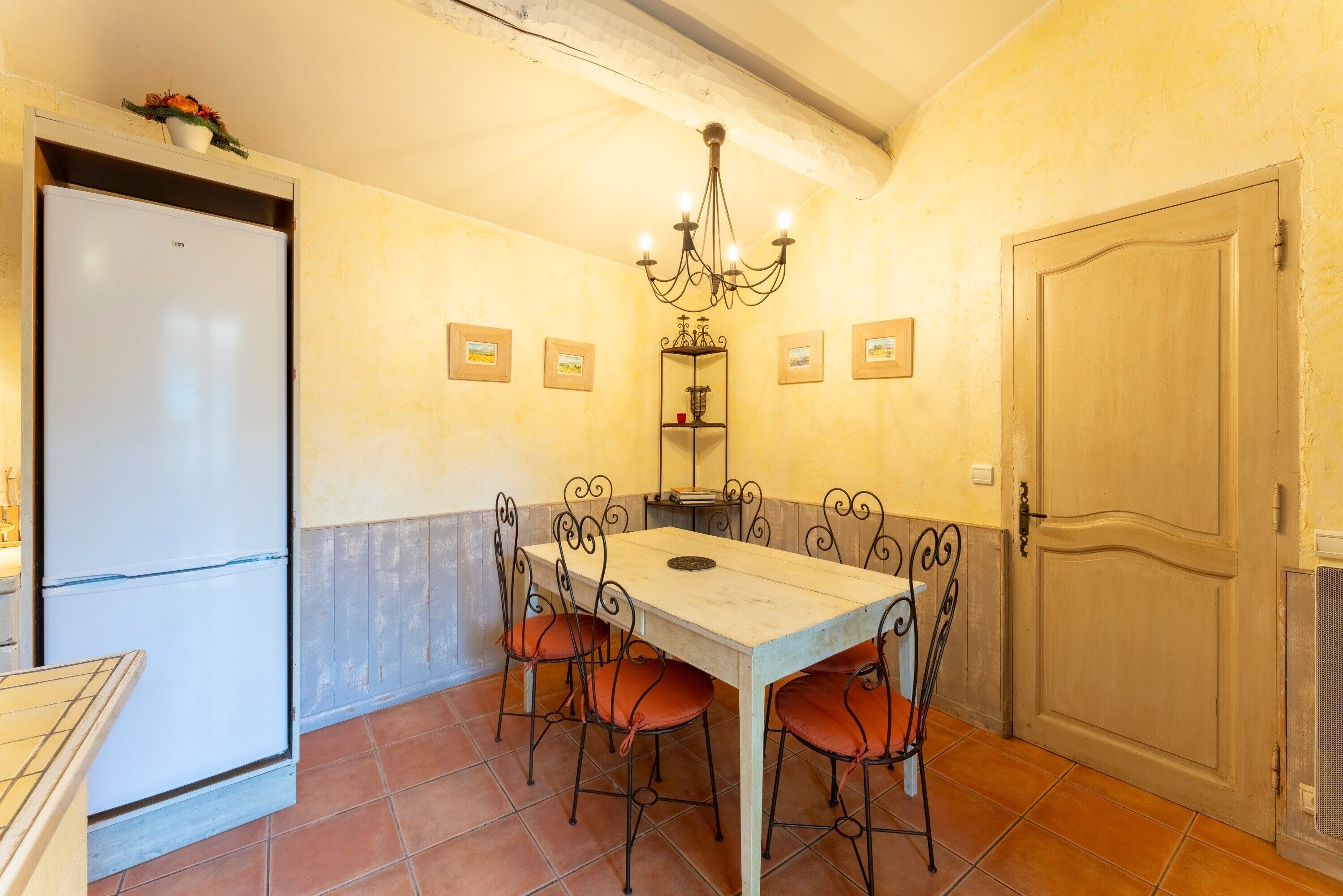 A dining area with a table and chairs, a chandelier, a refrigerator, and a door.