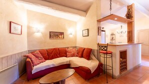 A cozy living area with a sectional sofa, a small round table, a bar area with a wine rack, and wall-mounted lighting. - Provençal House “Le Patio” – 2 Bedrooms, Private Terrace, Pool & Garden in Velleron (Velleron)