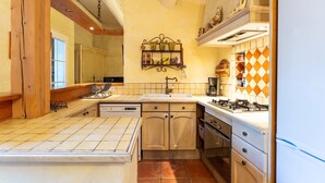A kitchen with a central island, wooden cabinets, a hanging spice rack, and a tiled backsplash. - Provençal House “Le Patio” – 2 Bedrooms, Private Terrace, Pool & Garden in Velleron (Velleron)