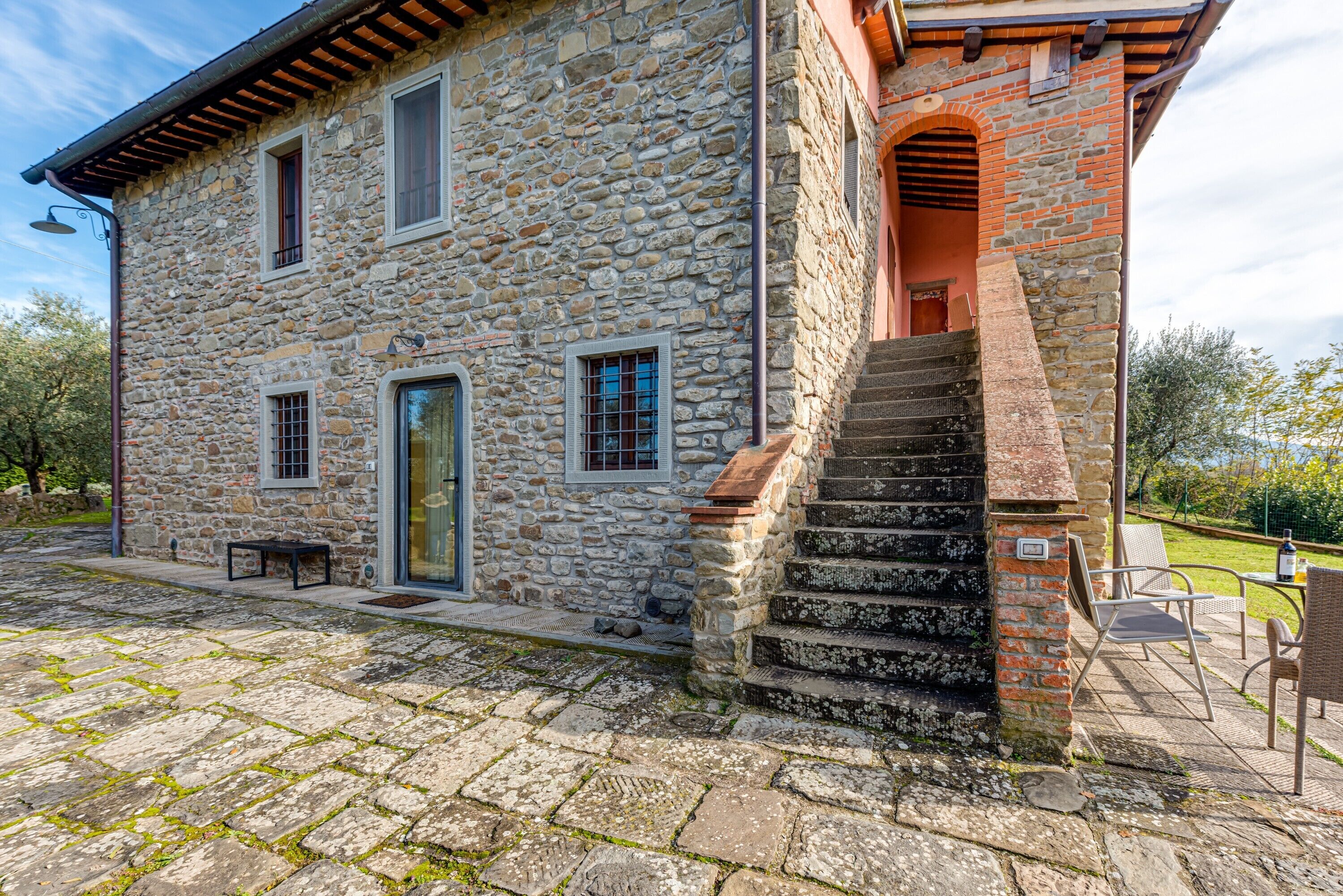 Un edificio de piedra con una escalera que lleva a una puerta, asientos exteriores y un patio empedrado.