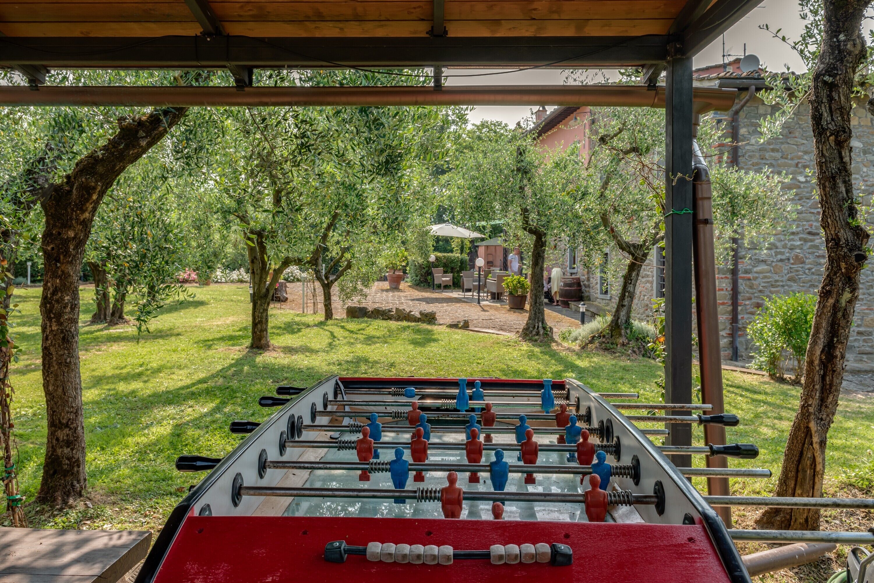 Ein Kicker-Tisch unter einer Holzw pergola mit Blick auf einen Garten und ein Gebäude im Hintergrund.