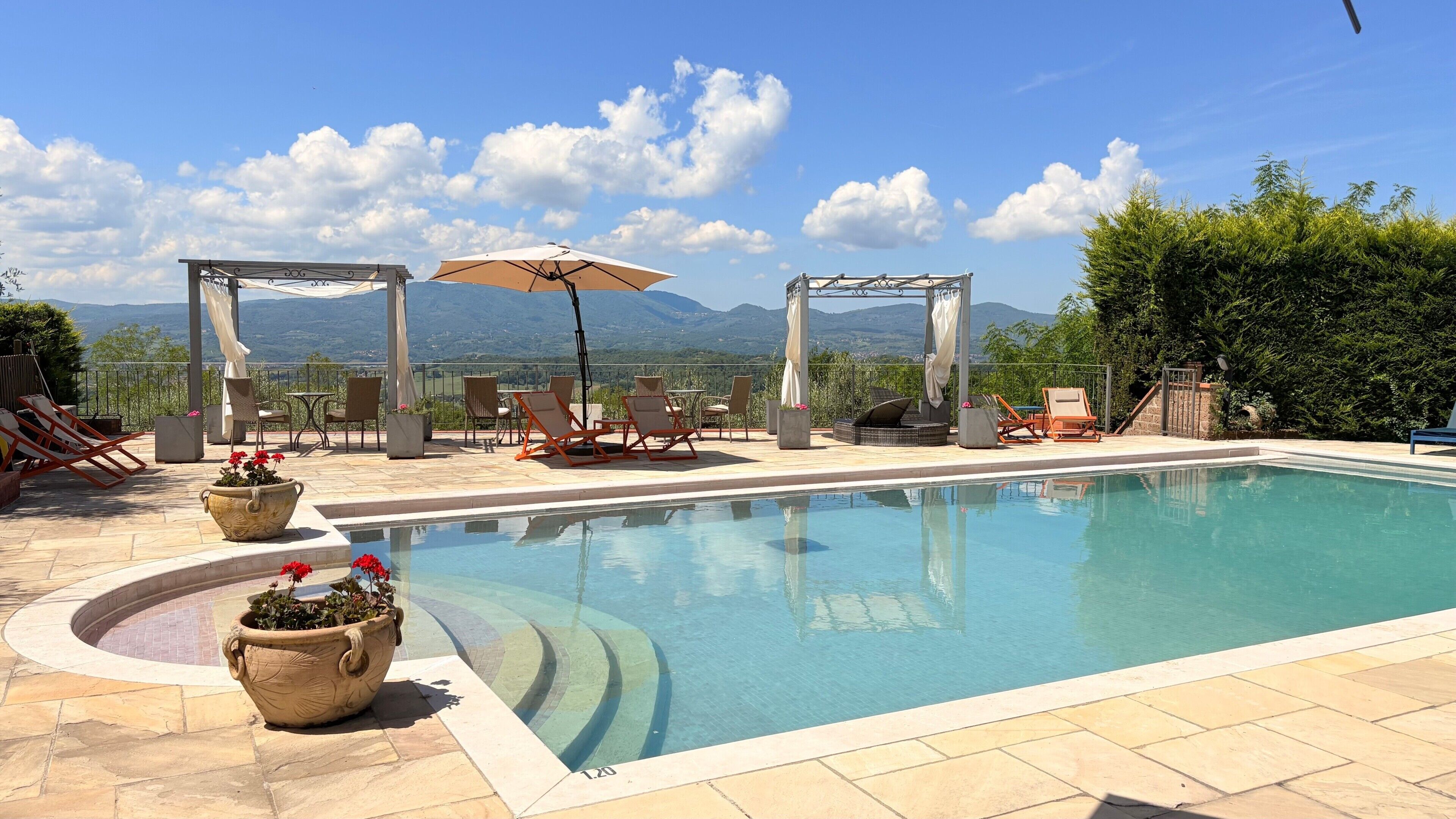 Une piscine dotée de chaises longues et de parasols, entourée d’un patio offrant une vue sur les montagnes.