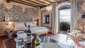 A bedroom with a stone wall, a bed, a table with glasses and a bottle, and a view of the outdoors. - Apartment 'Il Nido' with Shared Pool, Wi-Fi and Air Conditioning (Pian di Scò)