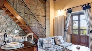 A cozy room with a wooden staircase, a checkered sofa, a dining table set with plates and glasses, and a window with curtains. - Apartment 'Il Belvedere' with Shared Pool, Private Terrace and Wi-Fi (Pian di Scò)