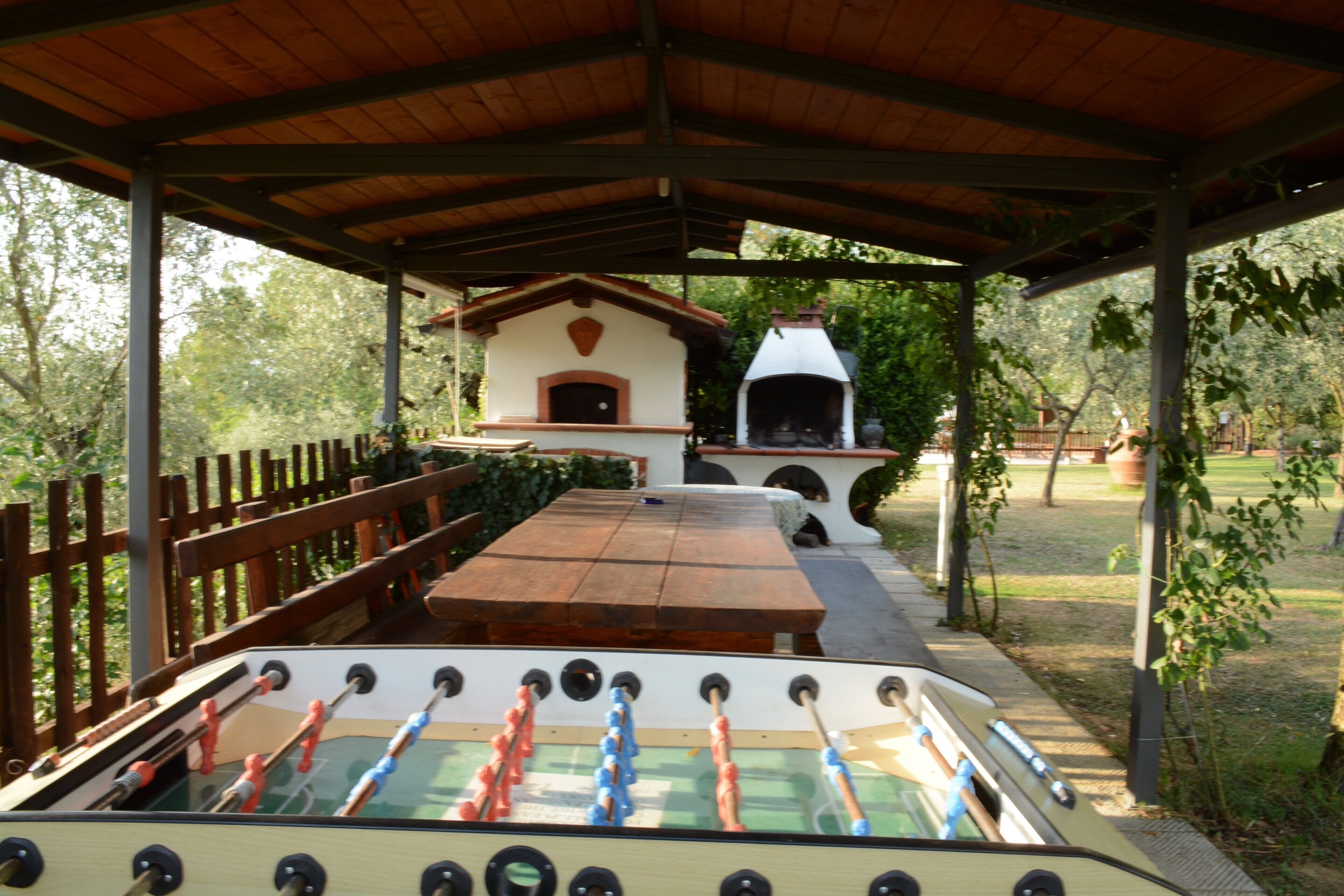 Un'area patio esterna con un tavolo da calcio, un barbecue e una zona salotto coperta.