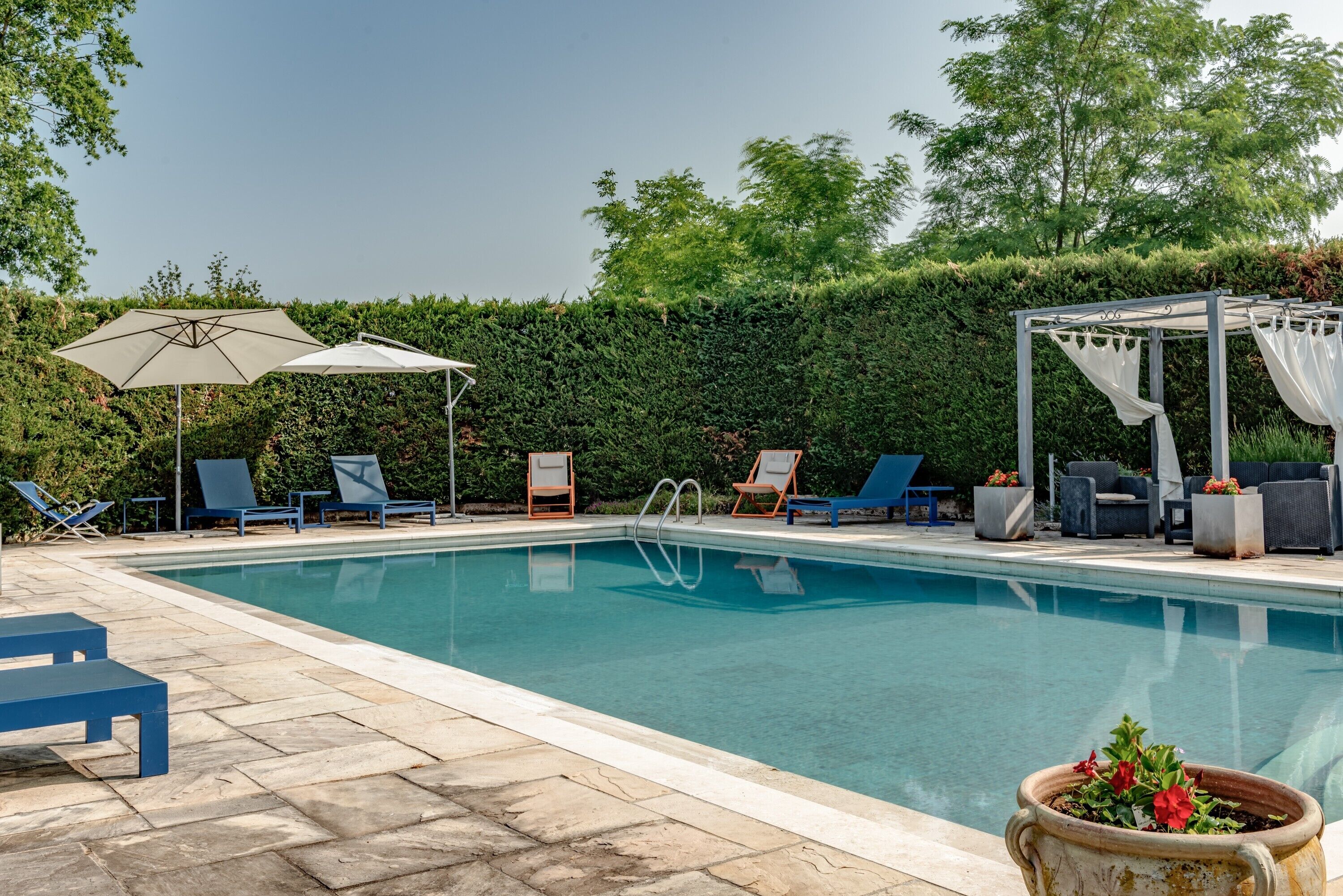 A swimming pool with lounge chairs, a pergola, and a hedge in the background.