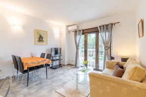 Una sala de estar con un sofá, una mesa de comedor con sillas, un televisor y una ventana con cortinas.