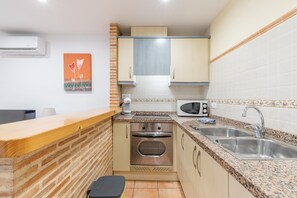 A compact kitchen with a microwave, oven, sink, and a wooden counter.