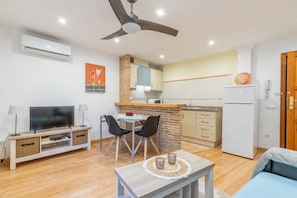 A modern living room with a flat-screen TV, a dining area, and a kitchen with a brick accent wall.