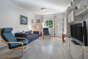 A living room with a sofa, two armchairs, a TV, and a window with curtains.