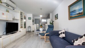Un salon équipé d’un téléviseur à écran plat, d’un canapé bleu et d’un coin repas avec des chaises et une table.