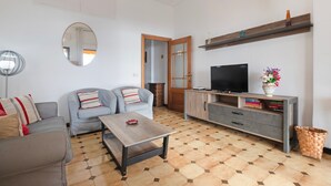 Una sala de estar con sofá, sillón, mesa de centro, televisor, estantería y espejo.