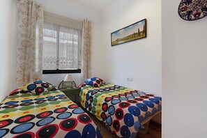 A bedroom with two beds, a window with sheer curtains, a desk with a chair, and a wall-mounted picture. - Apartment 'Ole Playa' with Sea View, Wi-Fi and Air Conditioning (Benalmadena)