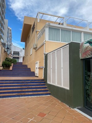 Un edificio residenziale con una scala che conduce a un ingresso chiuso da cancello, un balcone con ringhiera e cielo sereno.