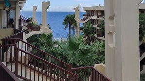 Un balcon offrant une vue sur la mer, les palmiers et l’architecture moderne.