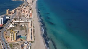 Vue aérienne d’une ville côtière avec une longue plage, de hauts immeubles et une mer bleue et limpide.