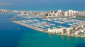 Vista aérea de un puerto deportivo con numerosas embarcaciones, edificios altos adyacentes y un mar azul y despejado.