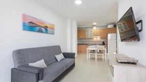 Una sala moderna con un sofá gris, una mesa de comedor y una cocina al fondo.