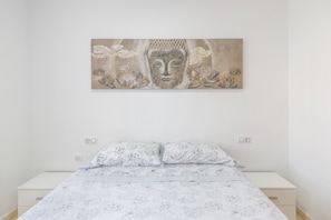 A bedroom with a bed, pillows, a nightstand, and a wall-mounted artwork.
