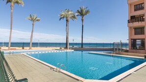 Una piscina con vista al océano, palmeras y un edificio con balcones.