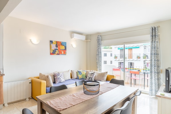 Ein modernes Wohnzimmer mit einer Couch, einem Esstisch und Stühlen. Ein Fenster bietet einen Ausblick nach draußen.