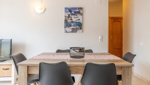 Zona pranzo con tavolo in legno, sedie nere, un quadro appeso alla parete e un televisore a sinistra.