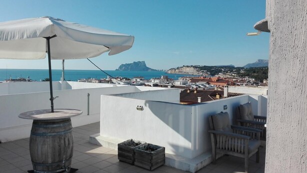 Una terrazza sul tetto con un ombrellone bianco, una botte di legno, un tavolino e una sedia.