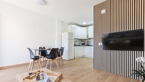 A modern kitchen with white cabinets, a flat-screen TV mounted on a striped wall, and a dining area with a wooden table and chairs. - Apartment 'Arena De 2 Mares' with Sea View, Shared Pool and Private Terrace (La Manga)