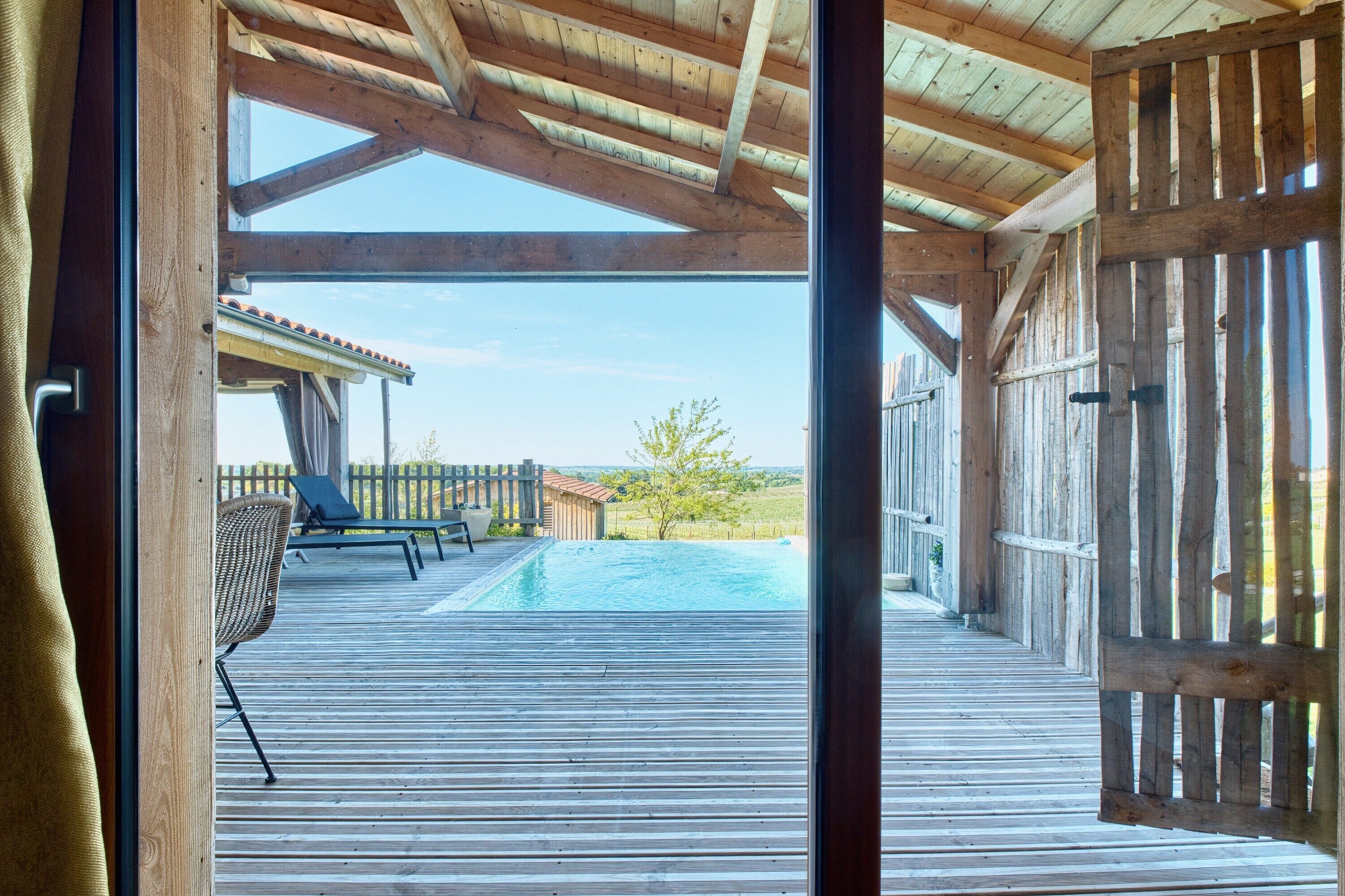A wooden deck with a pool, outdoor furniture, and a view of the landscape.