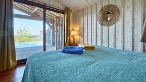 Ein Schlafzimmer mit einem großen Bett, einer Holzbalkendecke, einem runden Spiegel und Blick ins Freie.