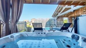 Ein Whirlpool mit Holzterrasse und Stühlen, ein Holzzaun und ein klarer Himmel.
