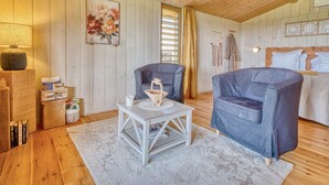 A cozy room with wooden walls, a bed with white bedding, a grey sofa, a small white table, and a lamp. - Cabin 'Muscadelle' with Shared Pool, Wi-Fi and Air Conditioning (Monbazillac)