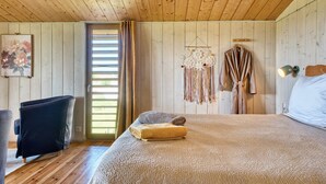 A wooden-paneled room with a bed, a chair, a door, and a wall decoration. - Cabin 'Muscadelle' with Shared Pool, Wi-Fi and Air Conditioning (Monbazillac)