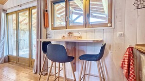 Un interior de madera con una zona de bar, dos sillas, un mostrador de madera y una ventana con cortinas.