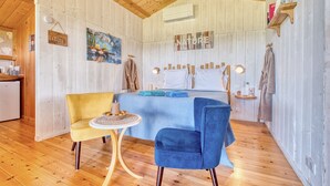 Una habitación con paneles de madera, una cama, dos sillas, una mesita peque ña y un estante en la pared.