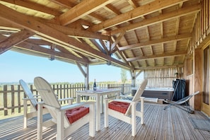 Eine Holzterrasse mit weißen Stühlen und einem Tisch, einem Whirlpool und Blick auf die Landschaft.