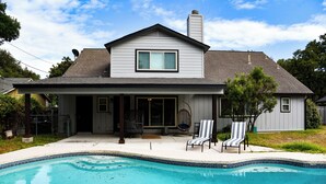 A two-story house with a swimming pool, a covered patio, and a large window. - 70s House Fun 6 Bedroom Pool Game Room (Round Rock)