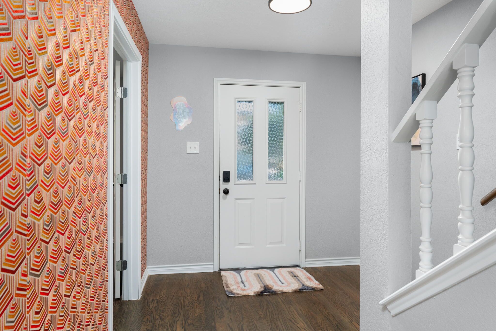 A hallway with a patterned wall, a white door with a glass panel, and a wooden floor.