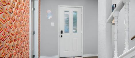 A hallway with a patterned wall, a white door with a glass panel, and a wooden floor.