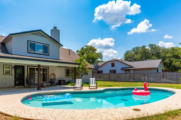 A backyard with a swimming pool, a house, and a wooden fence. - 70s House Fun 6 Bedroom Pool Game Room (Round Rock)