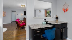 A modern kitchen with granite countertops, black cabinets, and a blue chair. - 70s House Fun 6 Bedroom Pool Game Room (Round Rock)