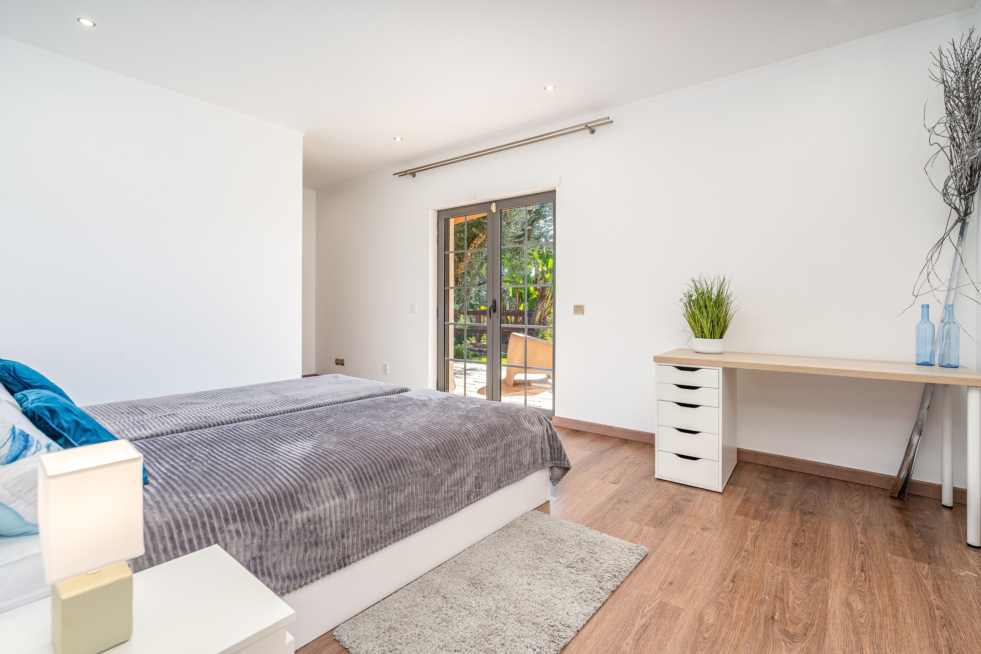 A modern bedroom with a bed, desk, and a sliding glass door to a balcony.