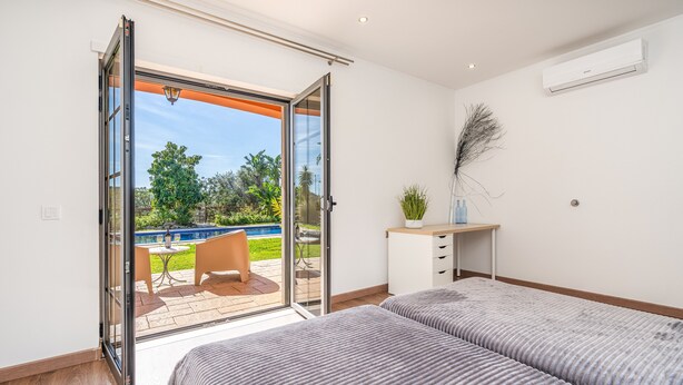 Ein Schlafzimmer mit zwei Betten, einem Schreibtisch und Blick auf eine Außenpatio mit einem Pool.