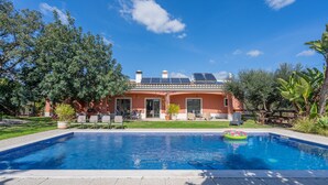 Ein Swimmingpool mit einem schwimmenden Ring, eine Terrasse mit Stühlen und ein Haus mit Solaranlage.