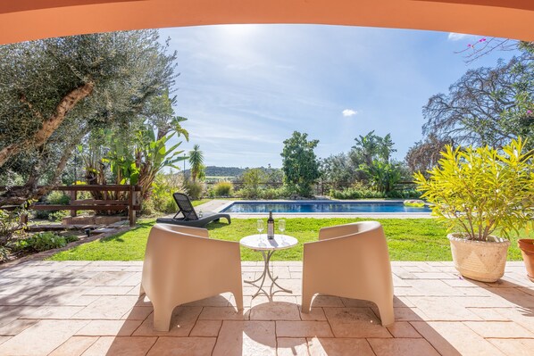 Un patio con dos sillas y una mesa, con vista a una piscina y un jardín.